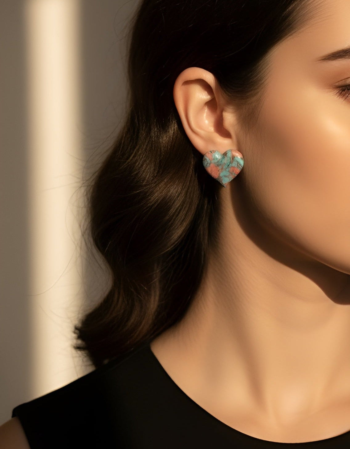 Close-up of a woman wearing turquoise heart-shaped earrings with a neutral background