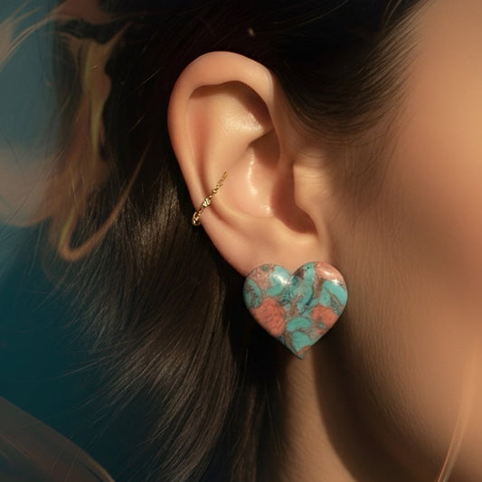Close-up of an ear wearing a turquoise heart-shaped earring with dark hair in the background.