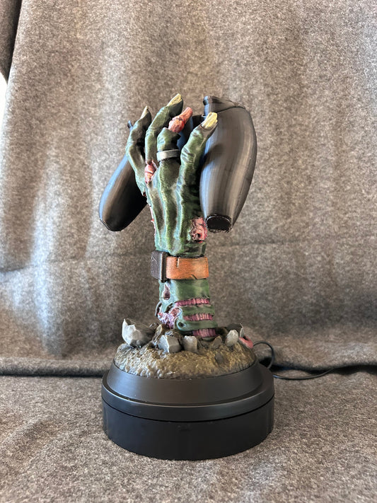 The zombie hand stand on its own, rising from grave dirt with a leather watch strap at the wrist.