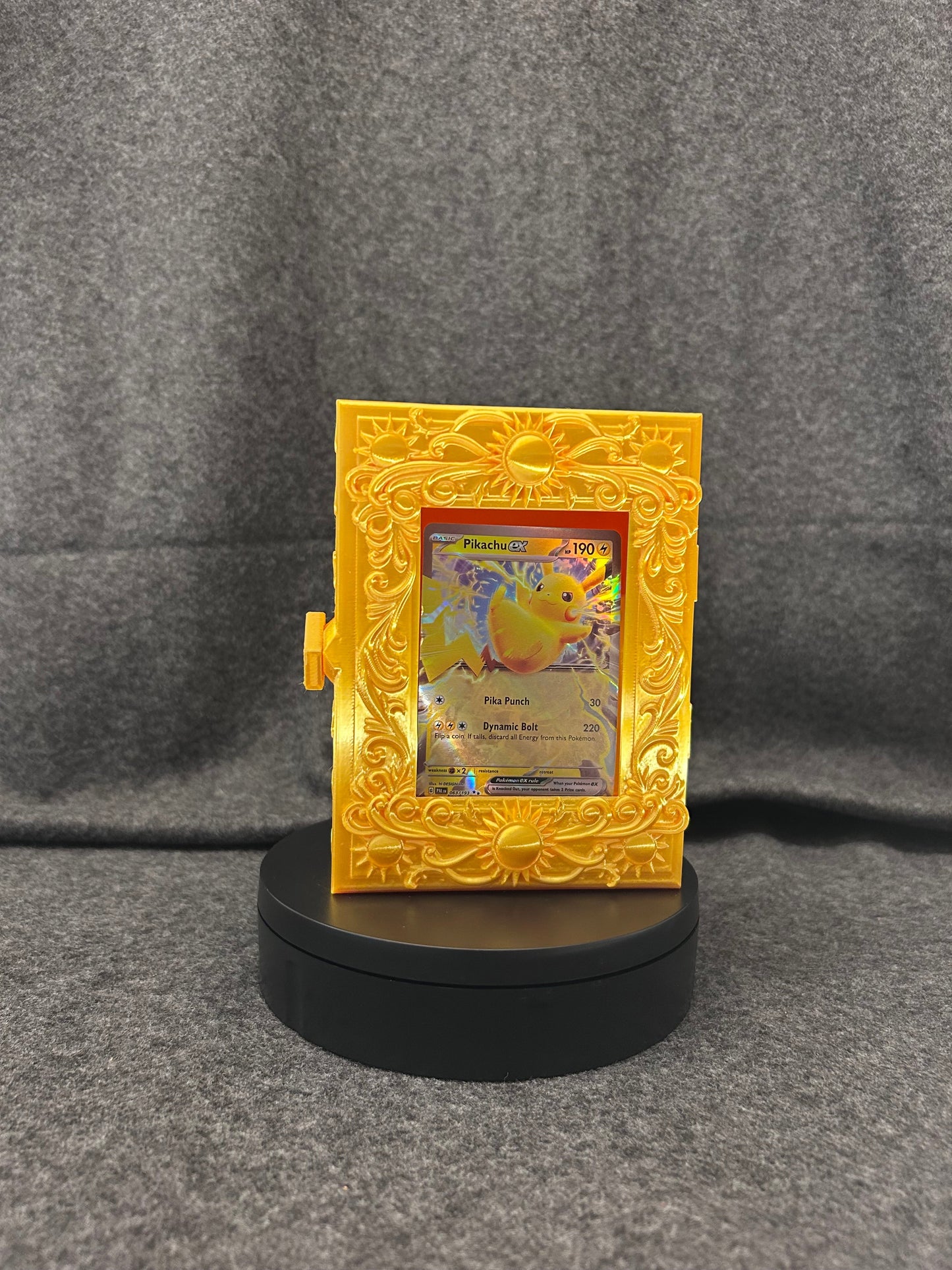 Gold card display case with sun medallions and baroque scrollwork, framing a single trading card.