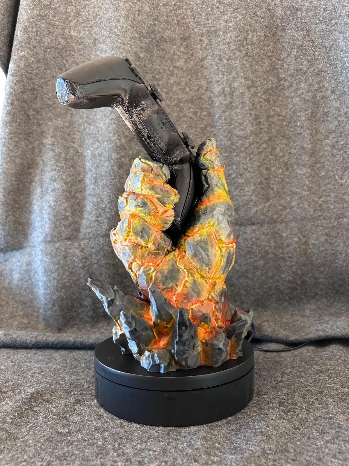 Hand-painted molten rock hand controller stand holding a game controller at playing angle.