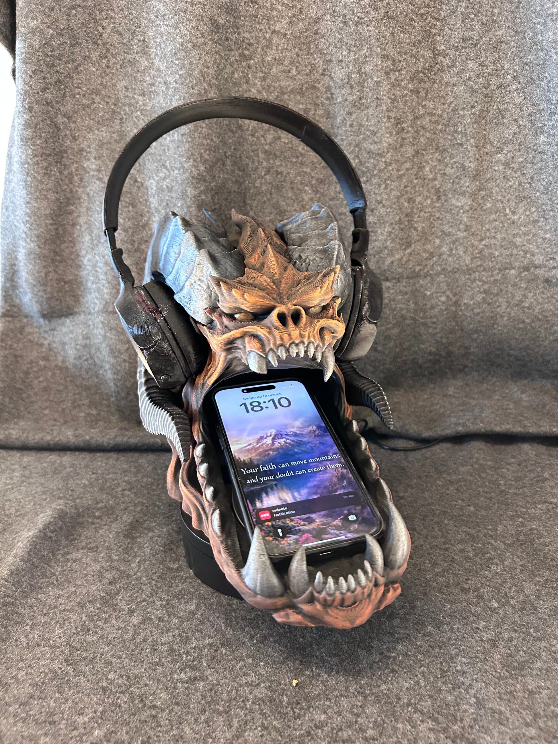 The dragon skull stand holding a headset, with a phone propped upright in its open jaw.