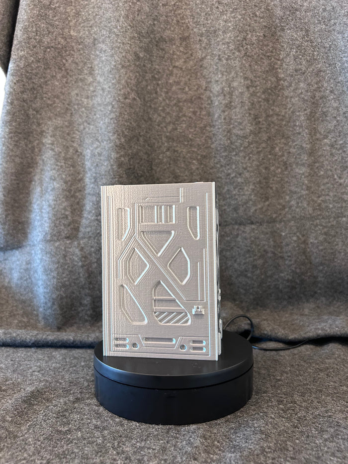 Sci-fi deck box printed in silver filament with panelled plating and a recessed skull sigil.