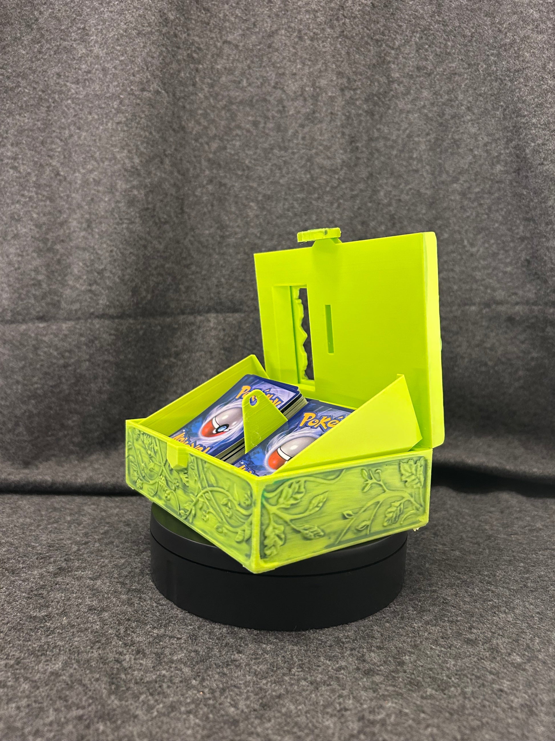 Lime green card display case carved with vines and leaves, hinged open with a trading card framed in the window.