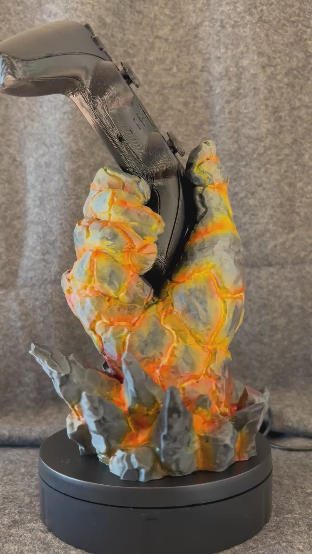 The Emberfist controller stand turning on a display stand, showing the glowing fissures in the painted basalt.